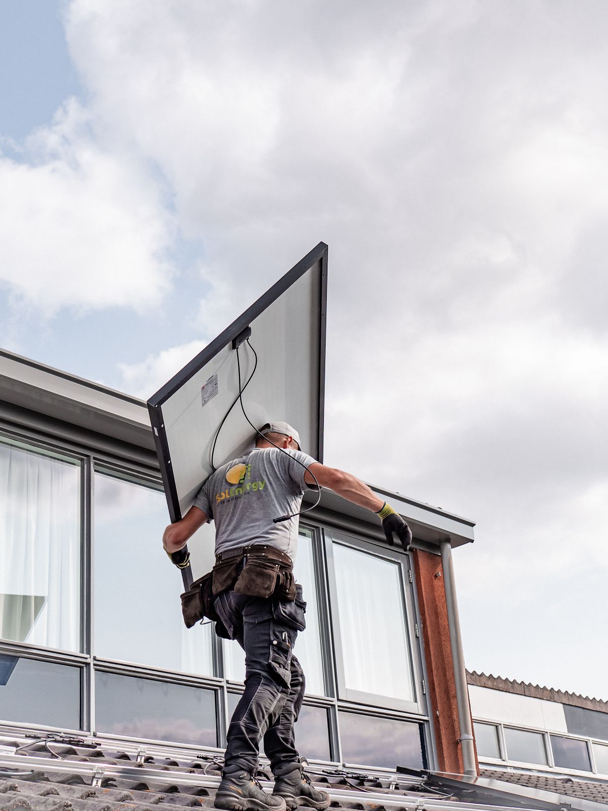 Technician carrying a full-size solar module across a rooftop